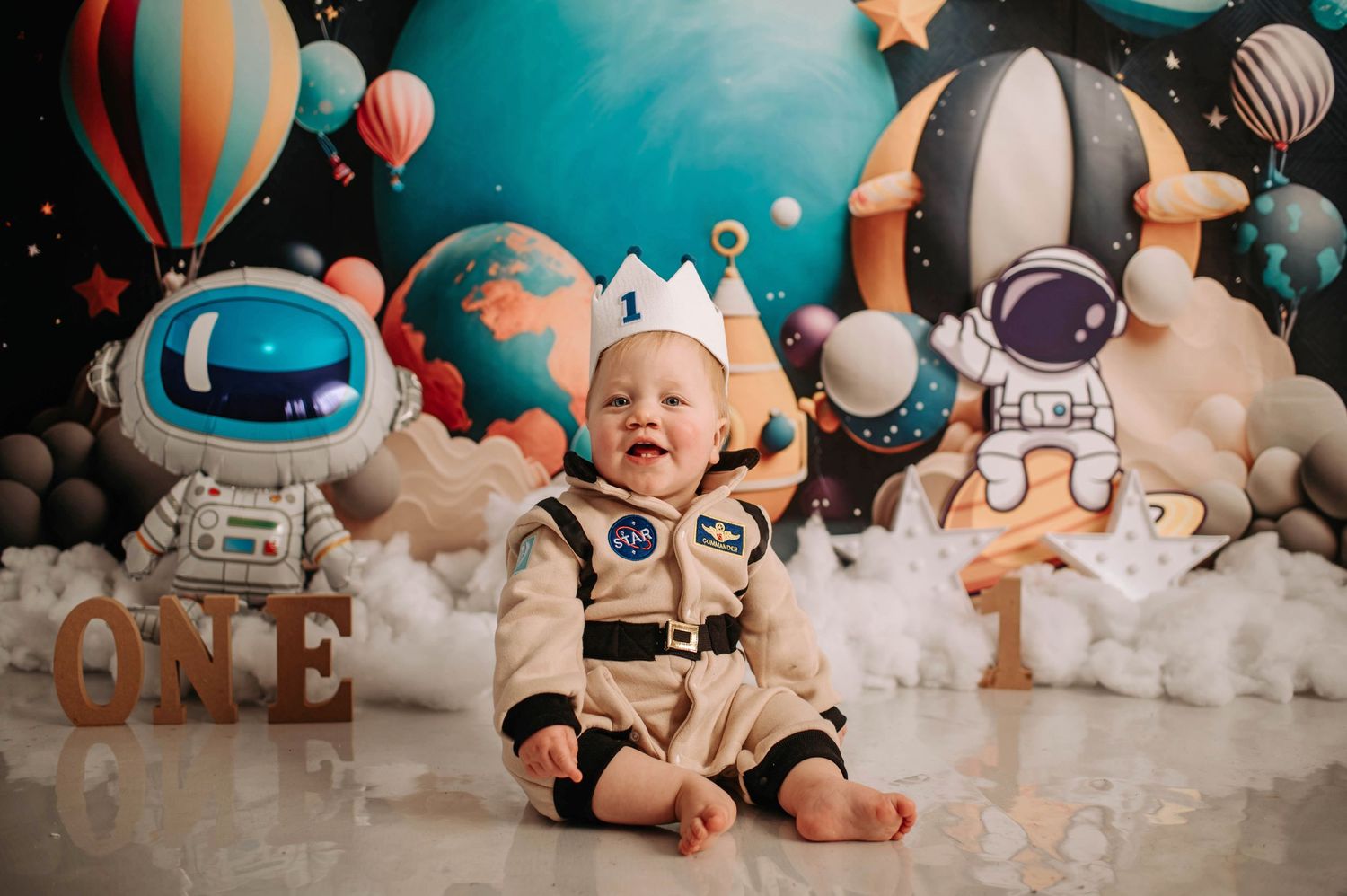 First birthday space-themed photo with astronaut suit and cosmic balloon decorations.