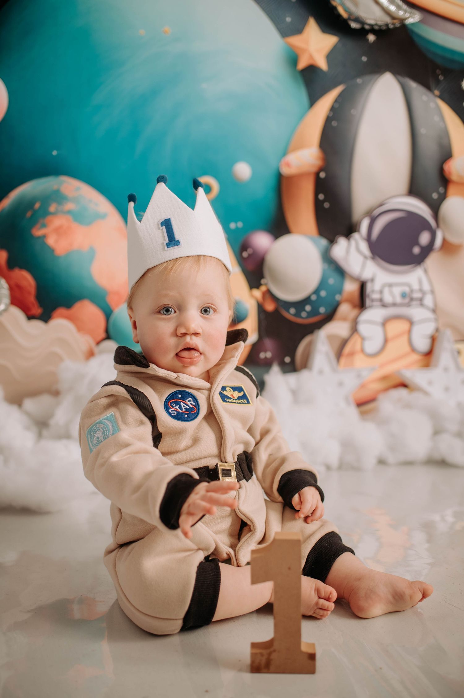 Space-themed first birthday setup with astronaut costume, crown, and planetary backdrop.