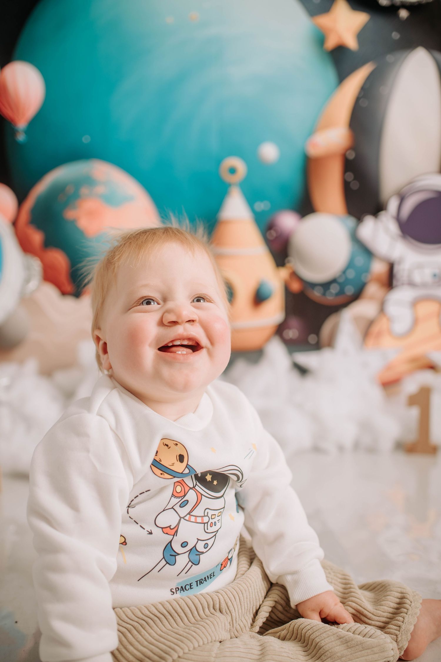 Smiling baby in white sweater with space print sitting against planetary backdrop.