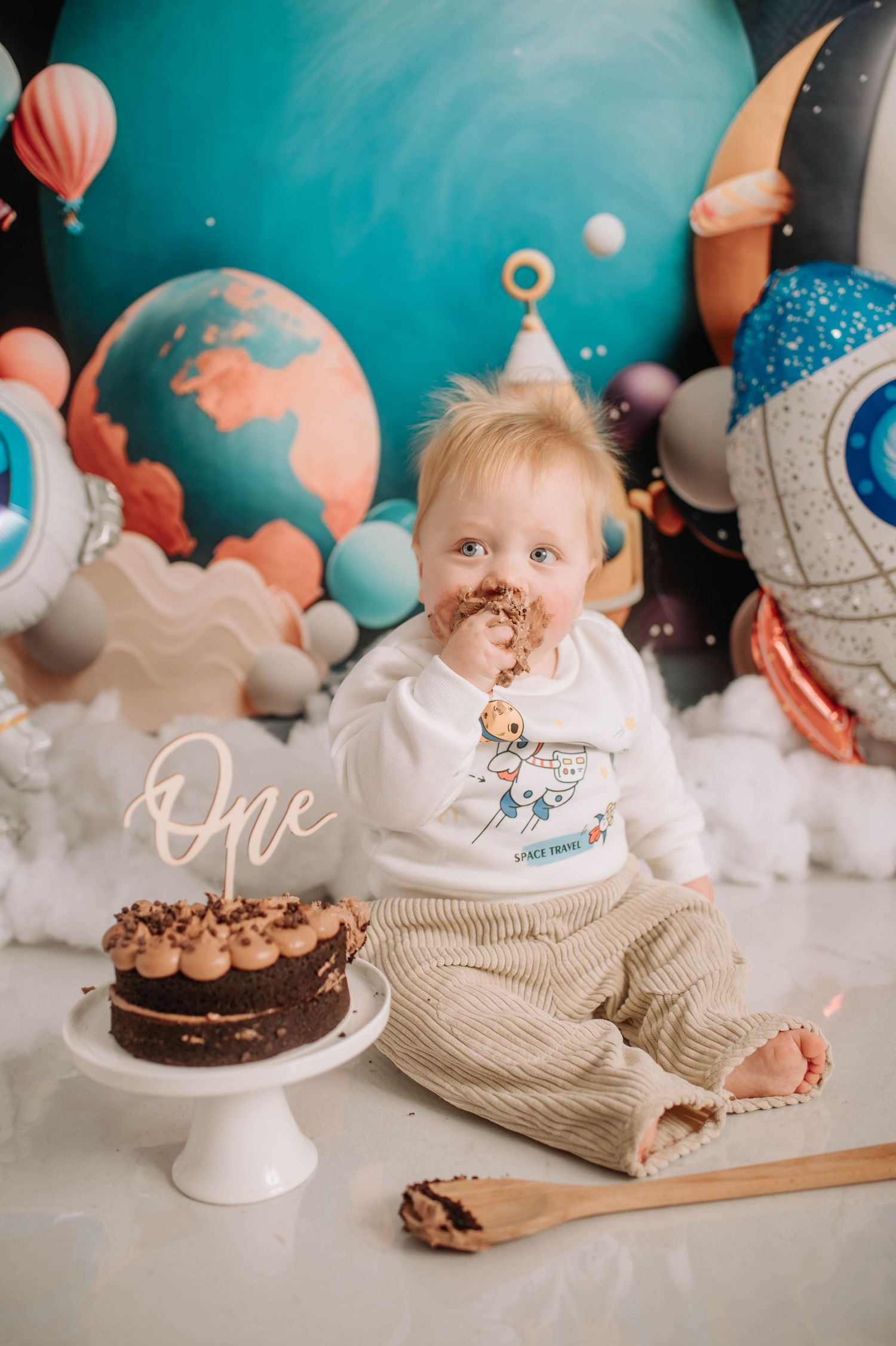 A first birthday cake smash photoshoot with space-themed decorations and chocolate cake.
