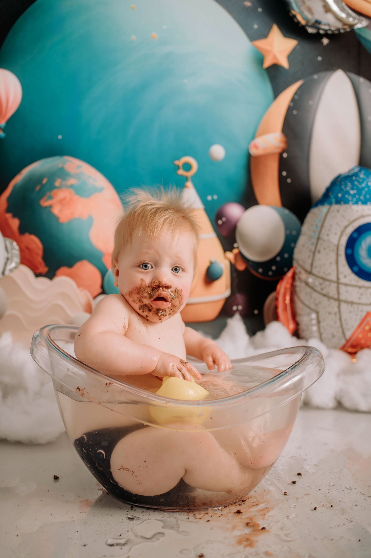 Messy cake smash photoshoot with space-themed background and clear bowl.
