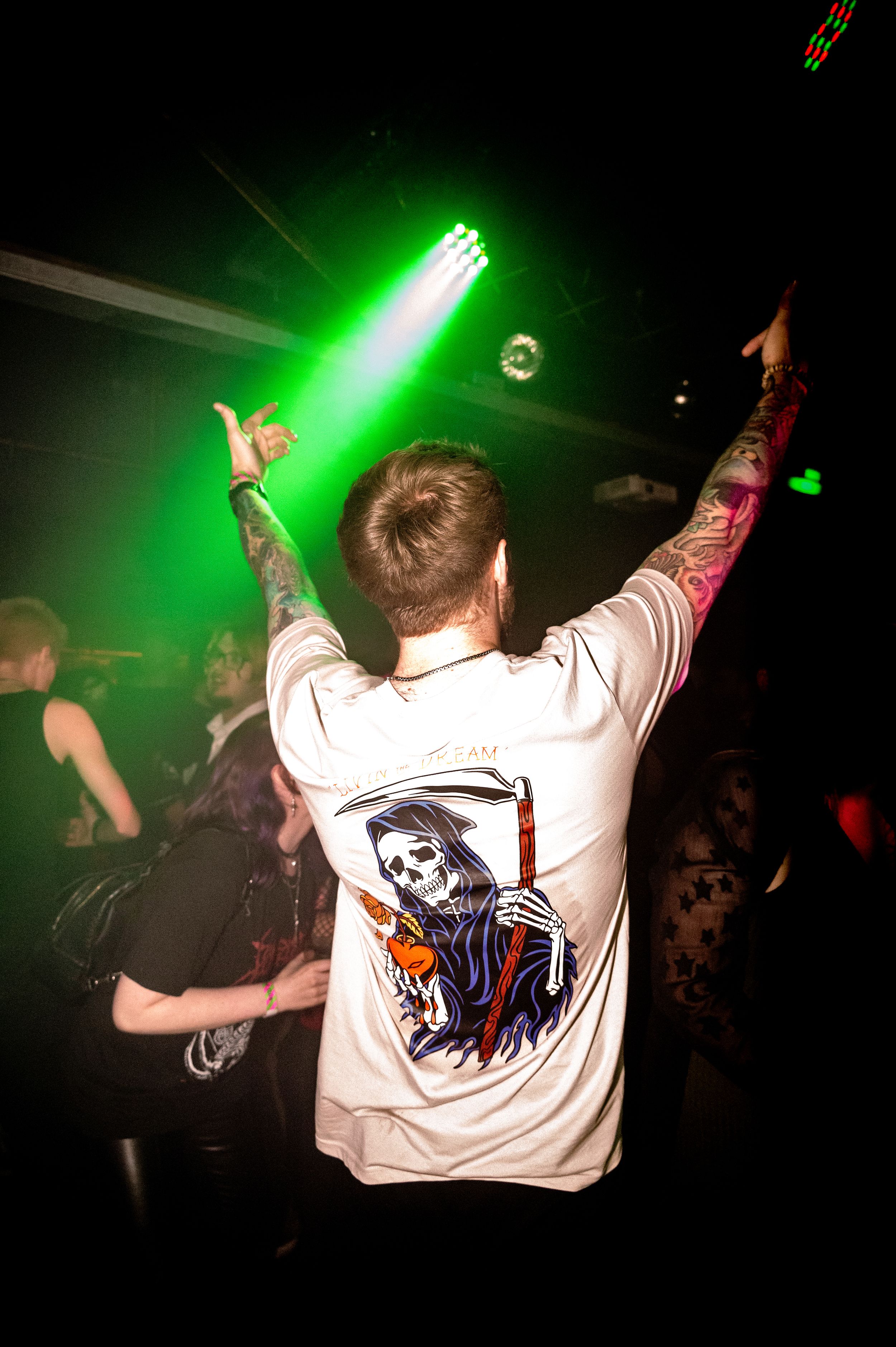 Person with skull graphic t-shirt dancing under green nightclub lights.
