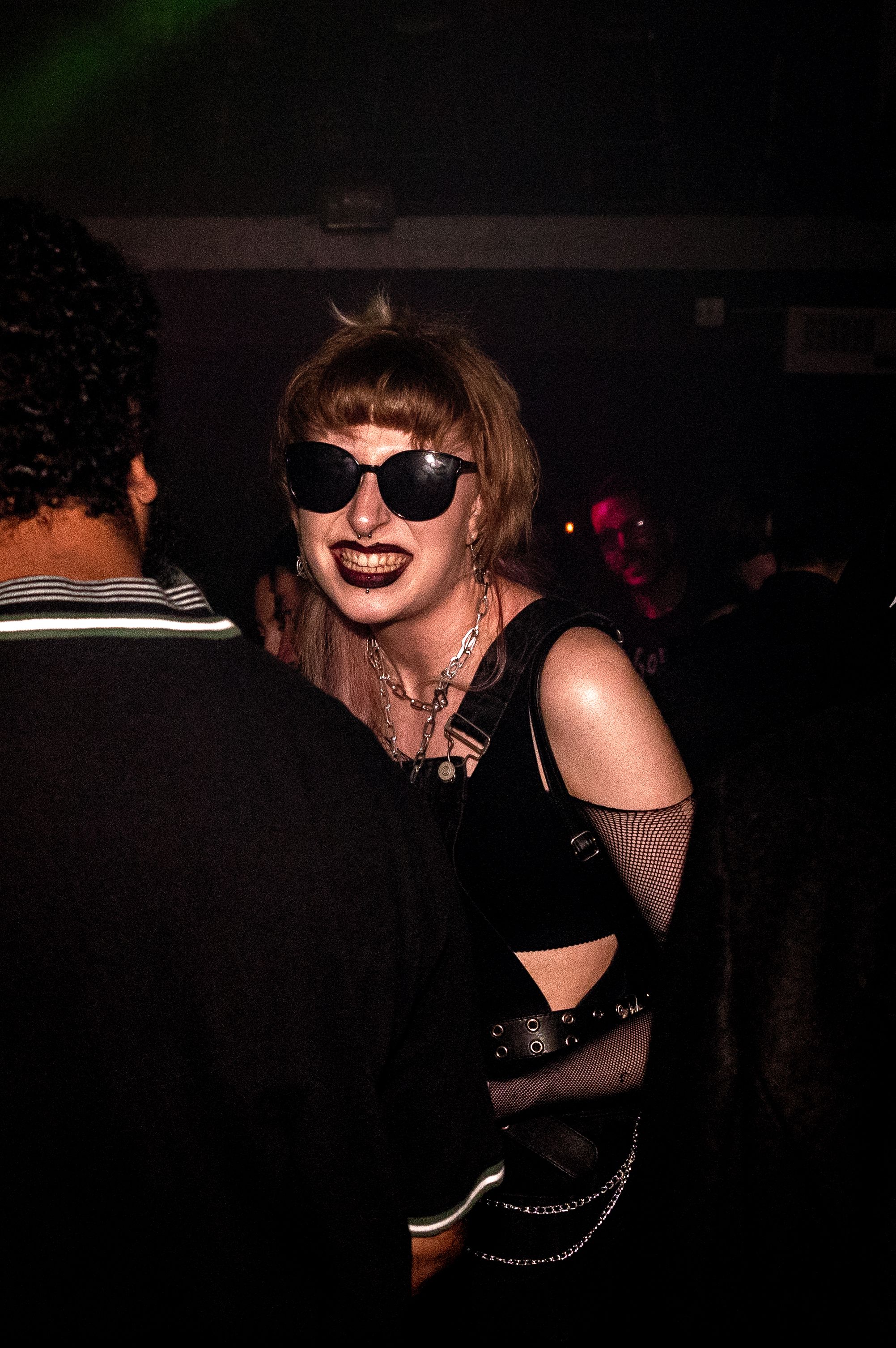 Alternative partygoer in sunglasses and dark outfit enjoying a nightclub atmosphere.