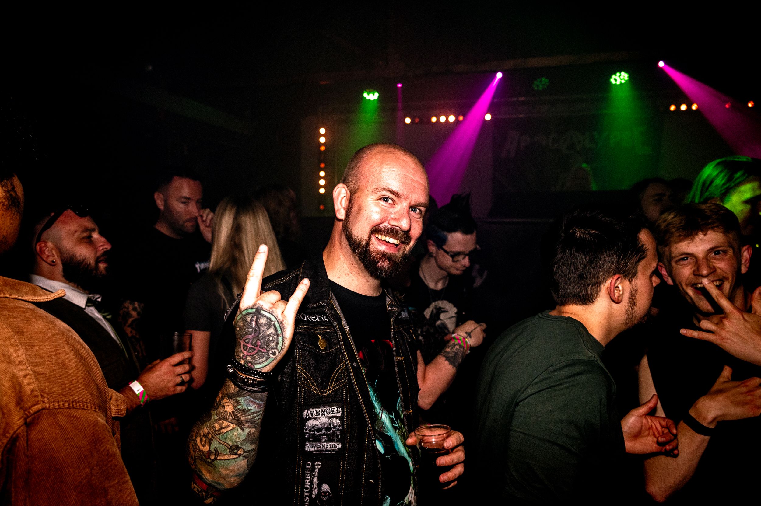 Enthusiastic partygoer making rock hand gesture under colorful club lights.