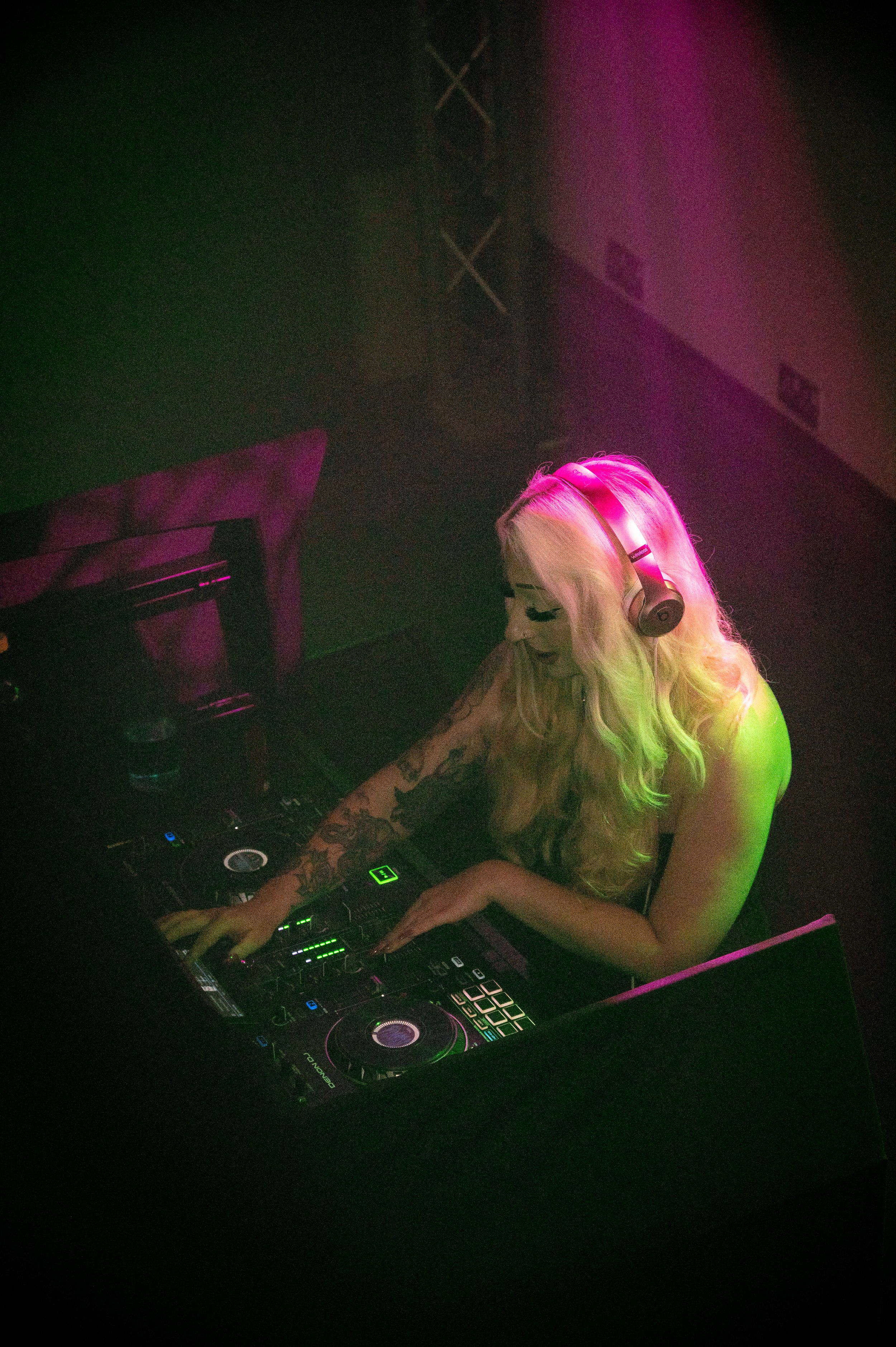 DJ performing at club setup with colorful pink and green lighting effects.