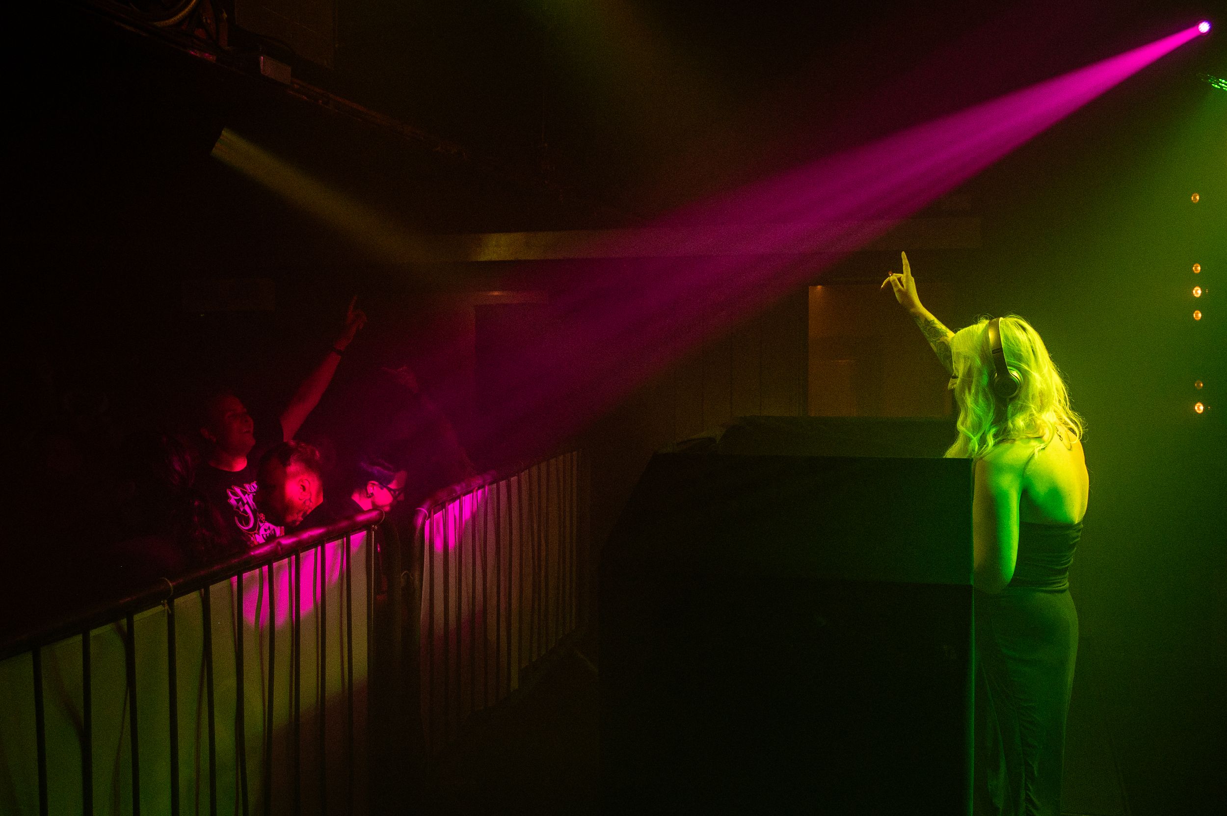 Performer illuminated by dramatic pink and green spotlights on elevated platform.