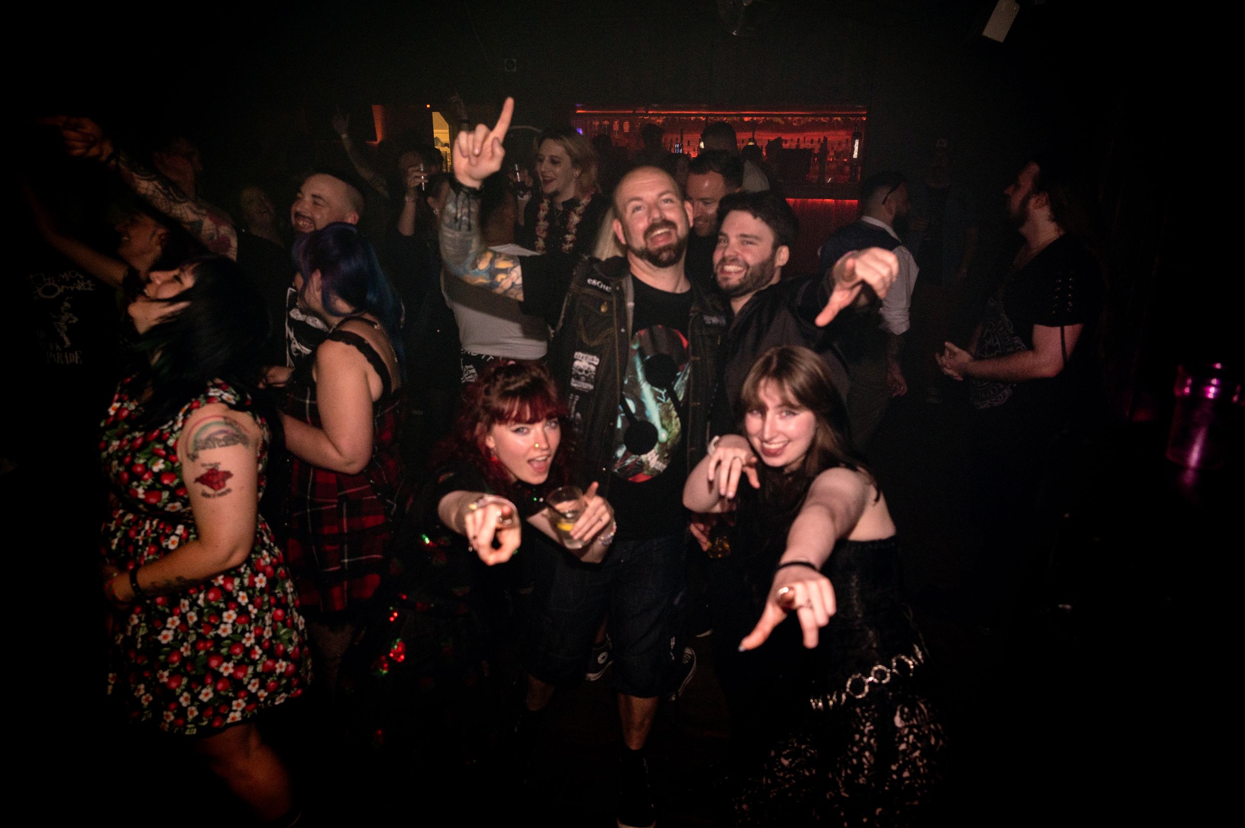 Group of energetic party-goers making rock gestures and posing together in a dark club setting.