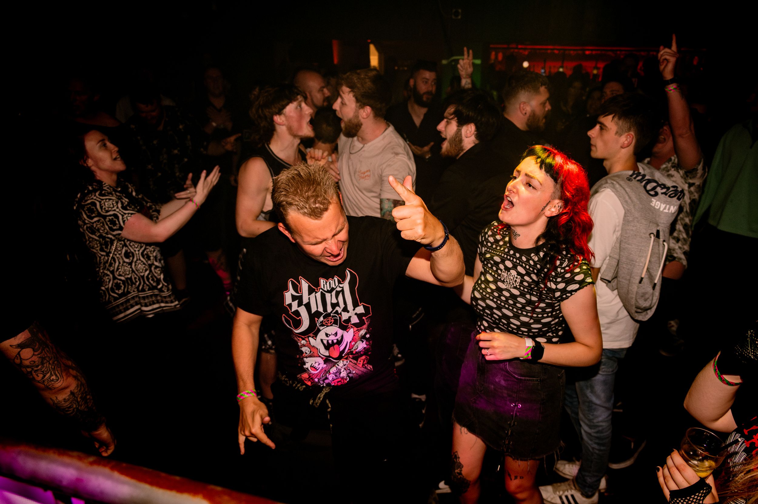 Concert attendees dancing and moving to music in a crowded venue with colorful lighting.