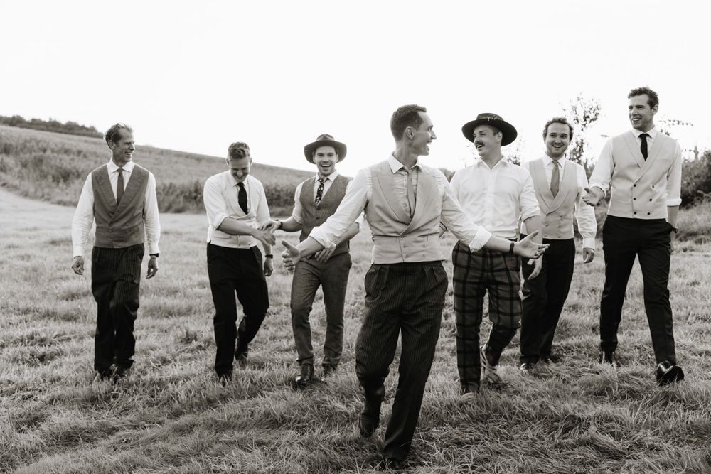 Black and white photo of groomsmen laughing together in an open field.