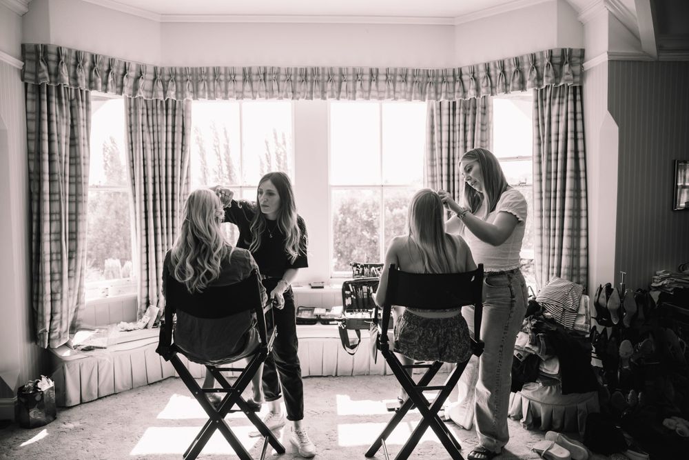 Black and white photo of wedding preparation scene with makeup chairs by a window.