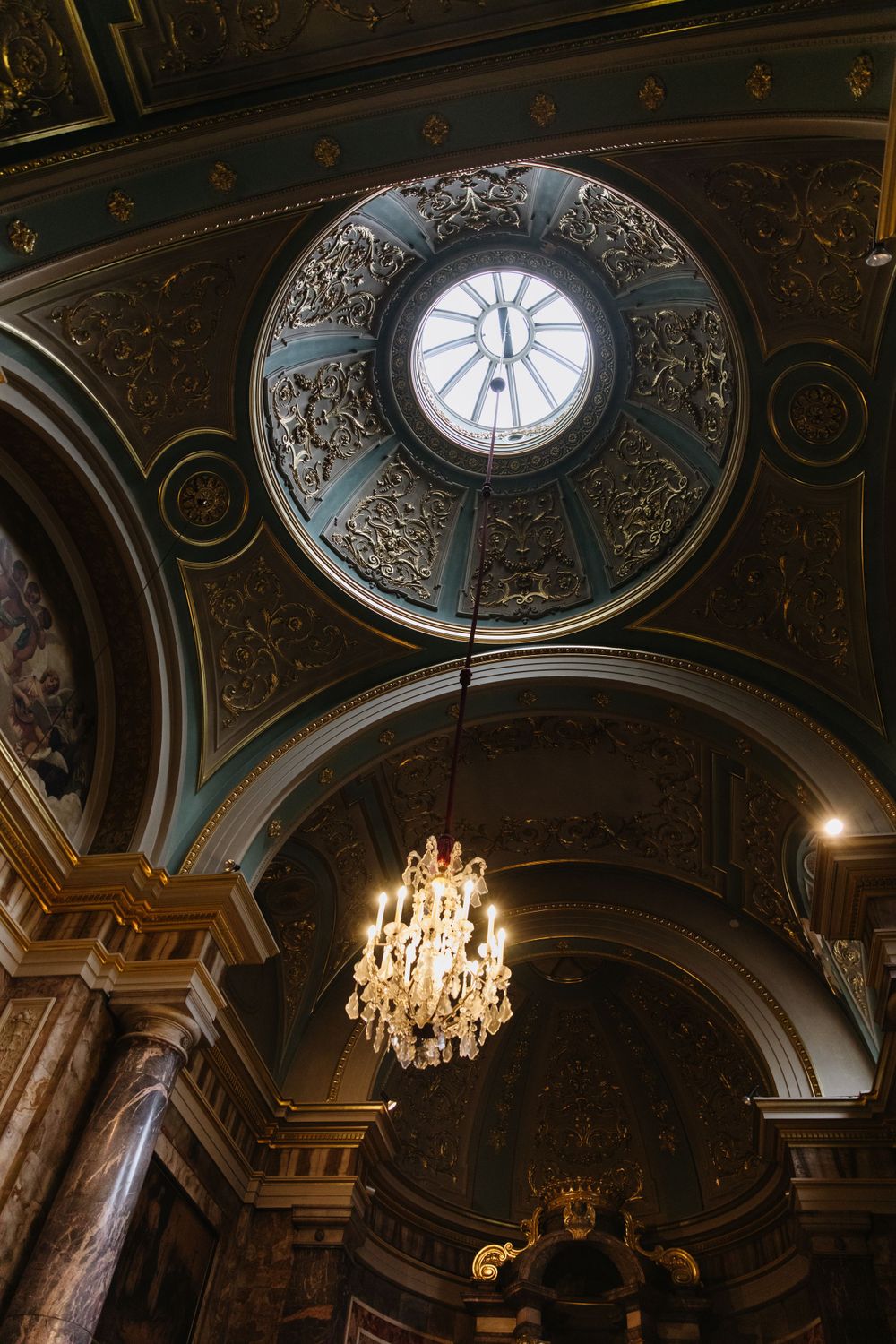 Ornate domed ceiling with crystal chandelier in historic building featuring intricate architectural details.