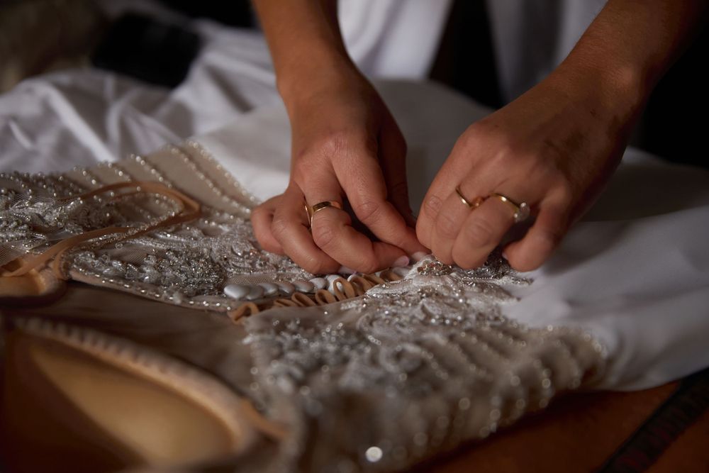 Close up of hands working on intricate beading details on delicate white fabric with scattered rhinestones.