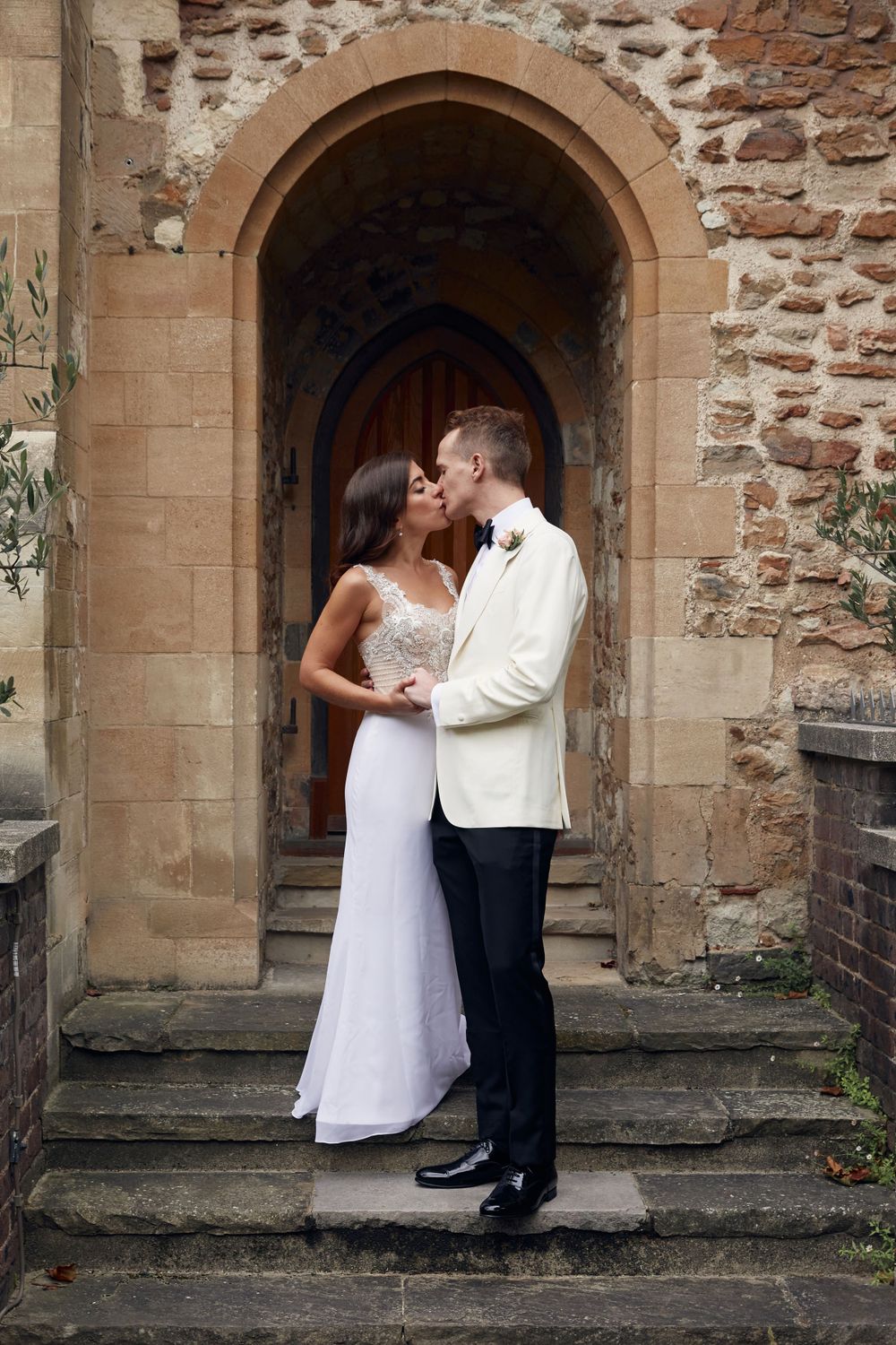 A romantic moment between newlyweds standing in an archway of a historic stone building.