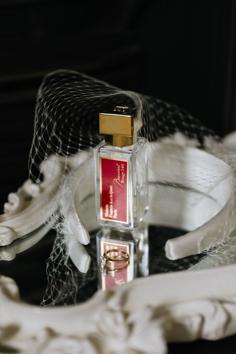 Elegant perfume bottle with gold cap displayed against dark background with delicate lace details.