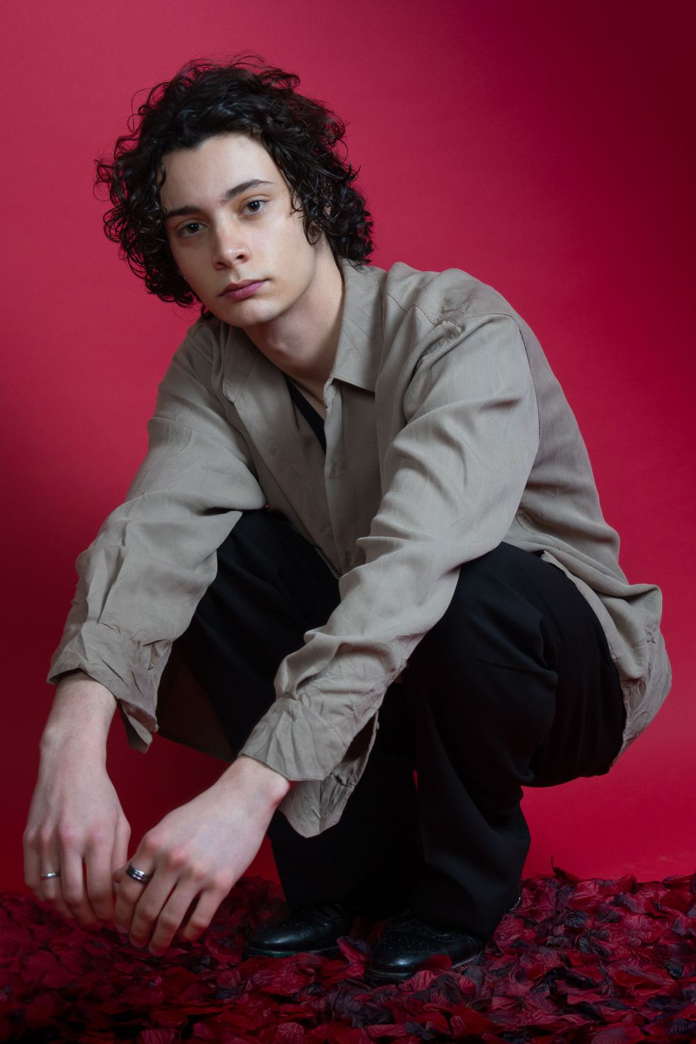 Portrait de mode en studio avec veste grise et pantalon noir sur fond rouge.