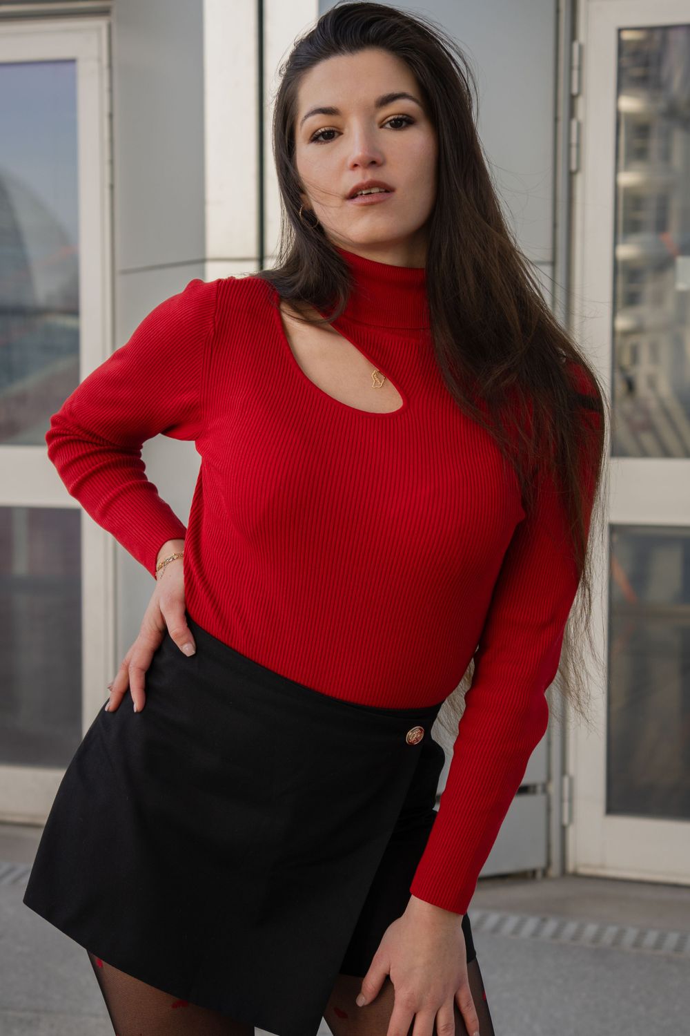 photographie d'une femme en pull col roulé rouge avec détails découpés et mini-jupe noire.