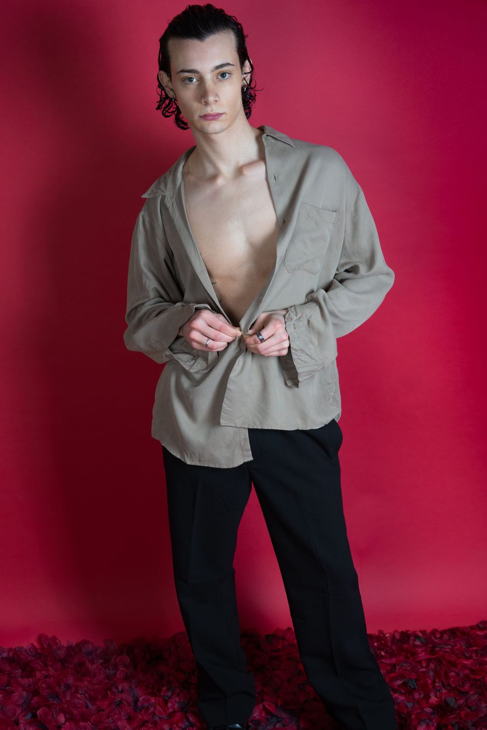 Portrait de mode montrant une veste grise déboutonnée et un pantalon noir sur fond rouge.