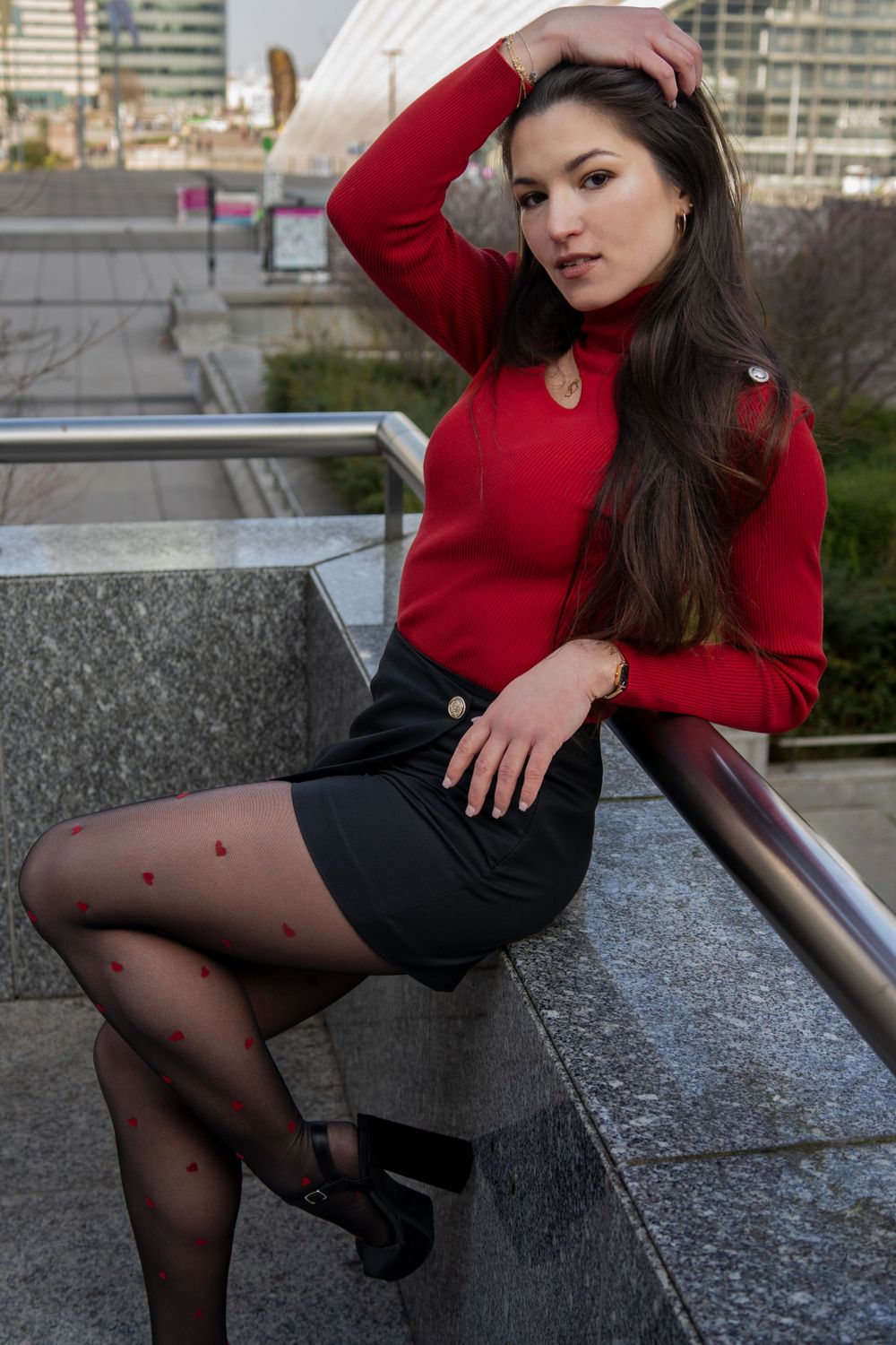 photographie d'un mannequin en pull rouge et jupe noire pose sur des marches architecturales extérieures pour le book du modèle.