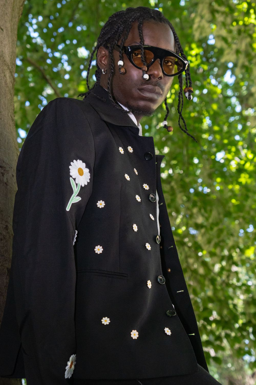 Person wearing a black jacket adorned with daisy flower embellishments against a green leafy background.