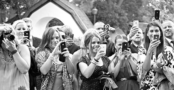 Black and white photo of wedding guests taking pictures with smartphones and cameras.