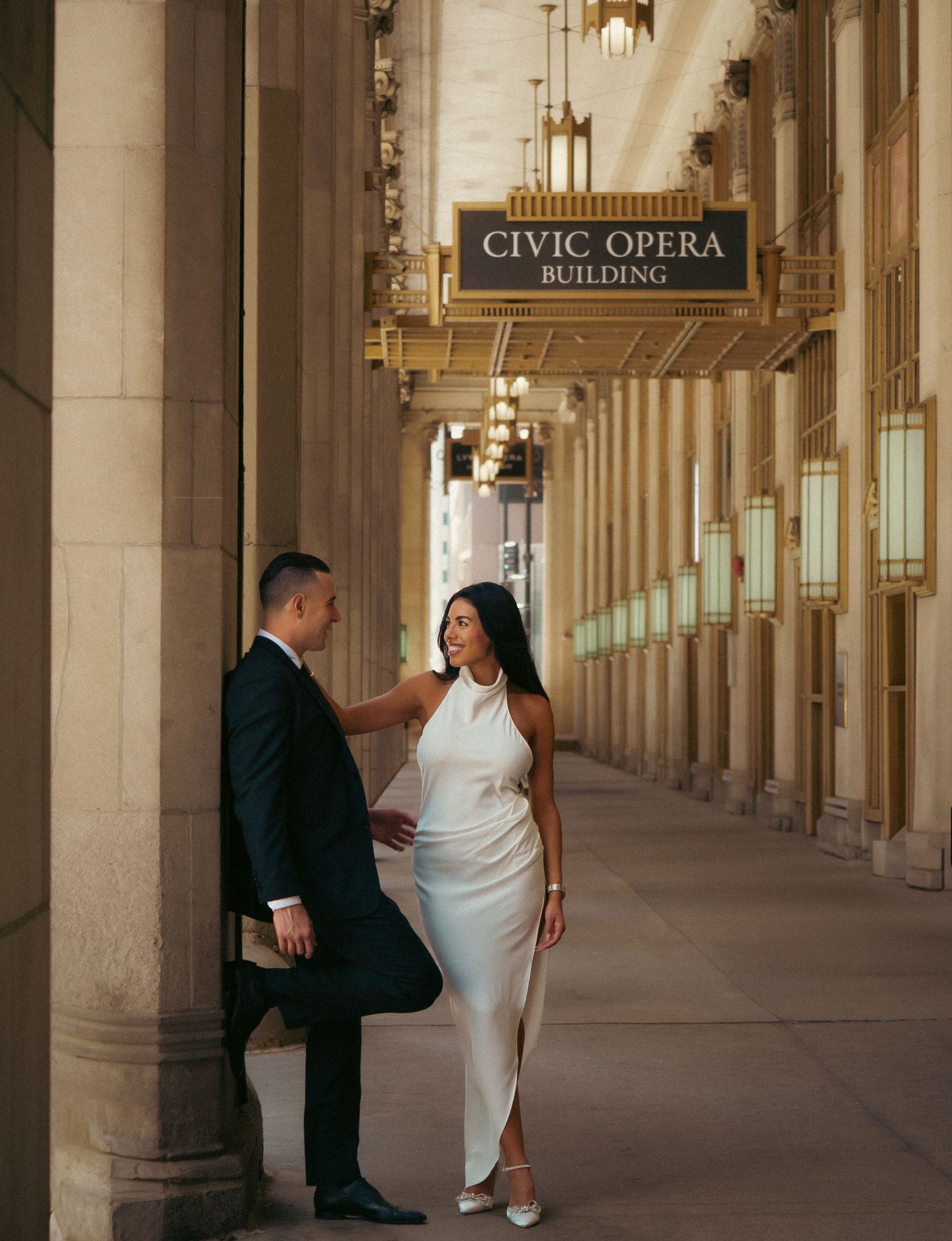 Elegant couple poses outside the Civic Opera Building with classic architecture.