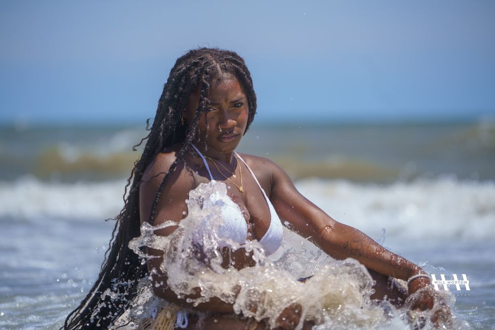 Person enjoys splashing in ocean waves wearing white beachwear on a sunny day.