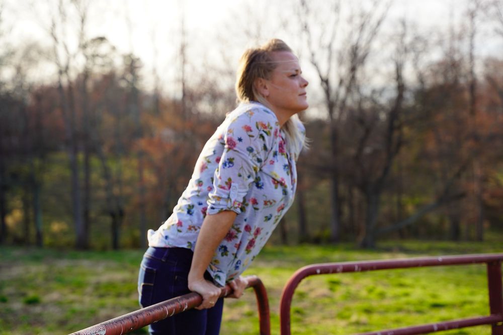 Person in floral shirt leaning against rustic farm fence during golden hour.