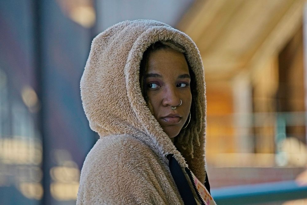Person wearing a cozy sherpa hoodie poses elegantly in front of a brick building.