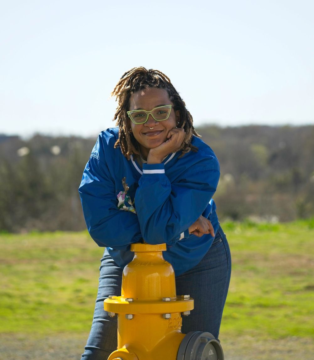 Person in blue jacket interacting with yellow industrial equipment in a grassy field.
