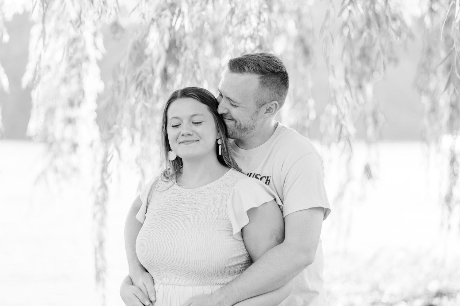 Black and white portrait showing a sweet interaction beneath willow trees.