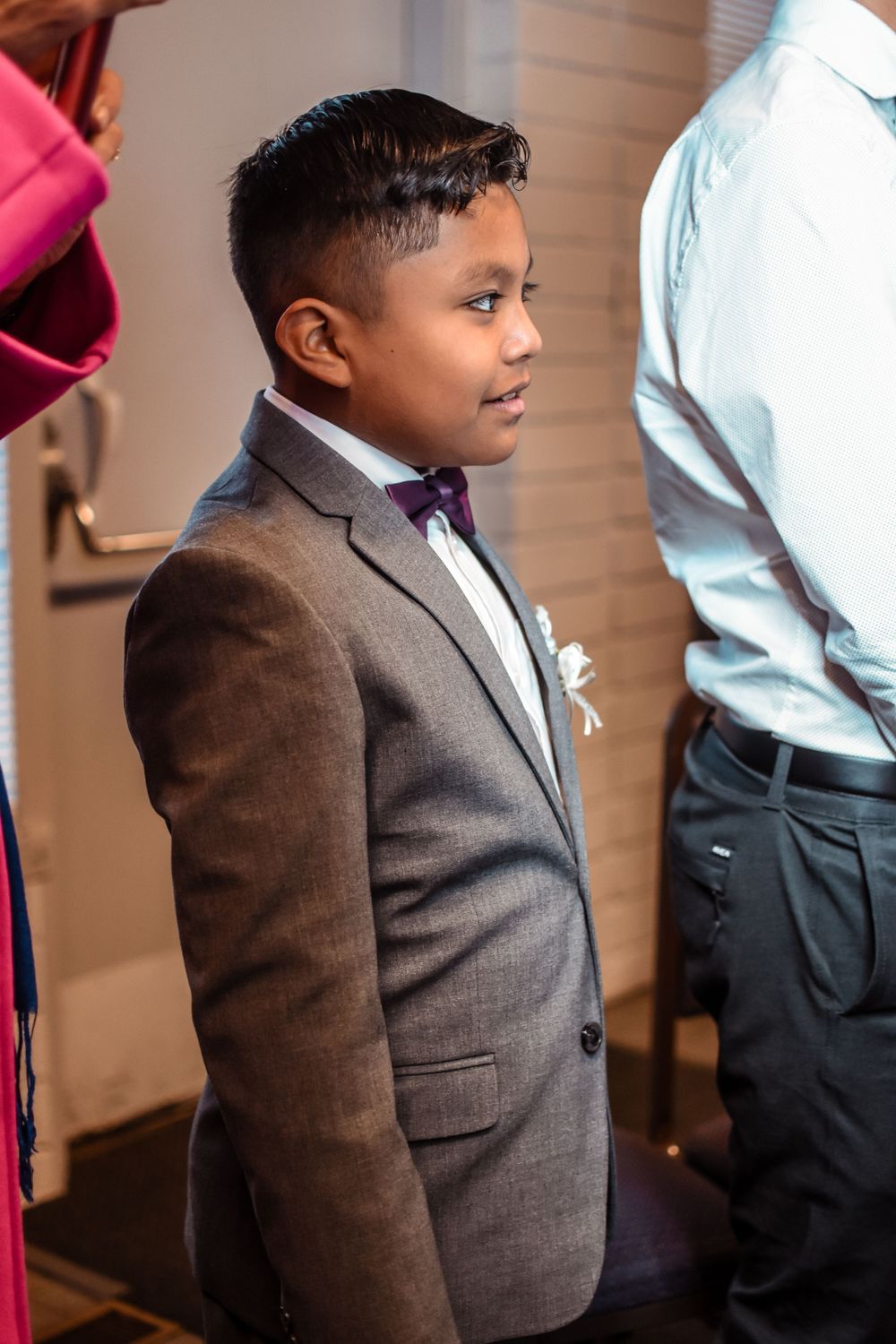 Young attendant in formal grey suit stands ready during wedding ceremony.