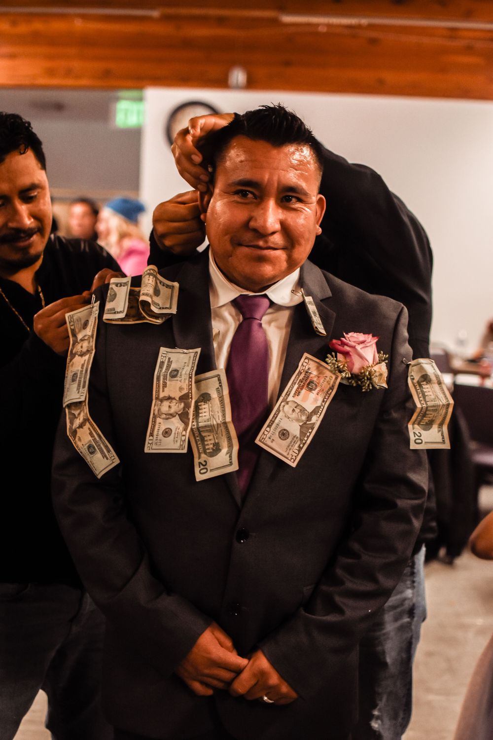 Wedding guest in dark suit decorated with dollar bills pinned to his jacket and purple tie.