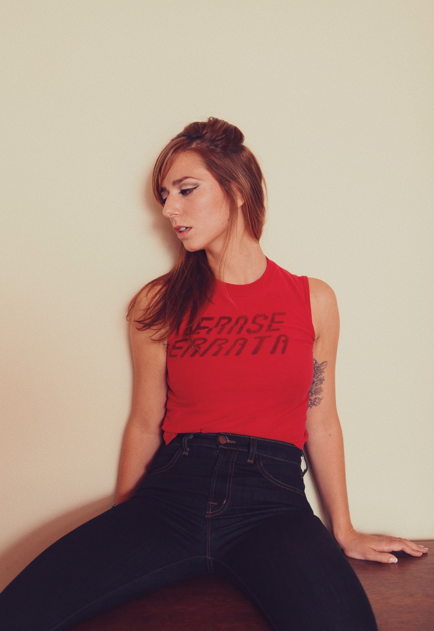 A figure in a red sleeveless top and dark jeans poses against a light colored wall in a series of artistic shots.