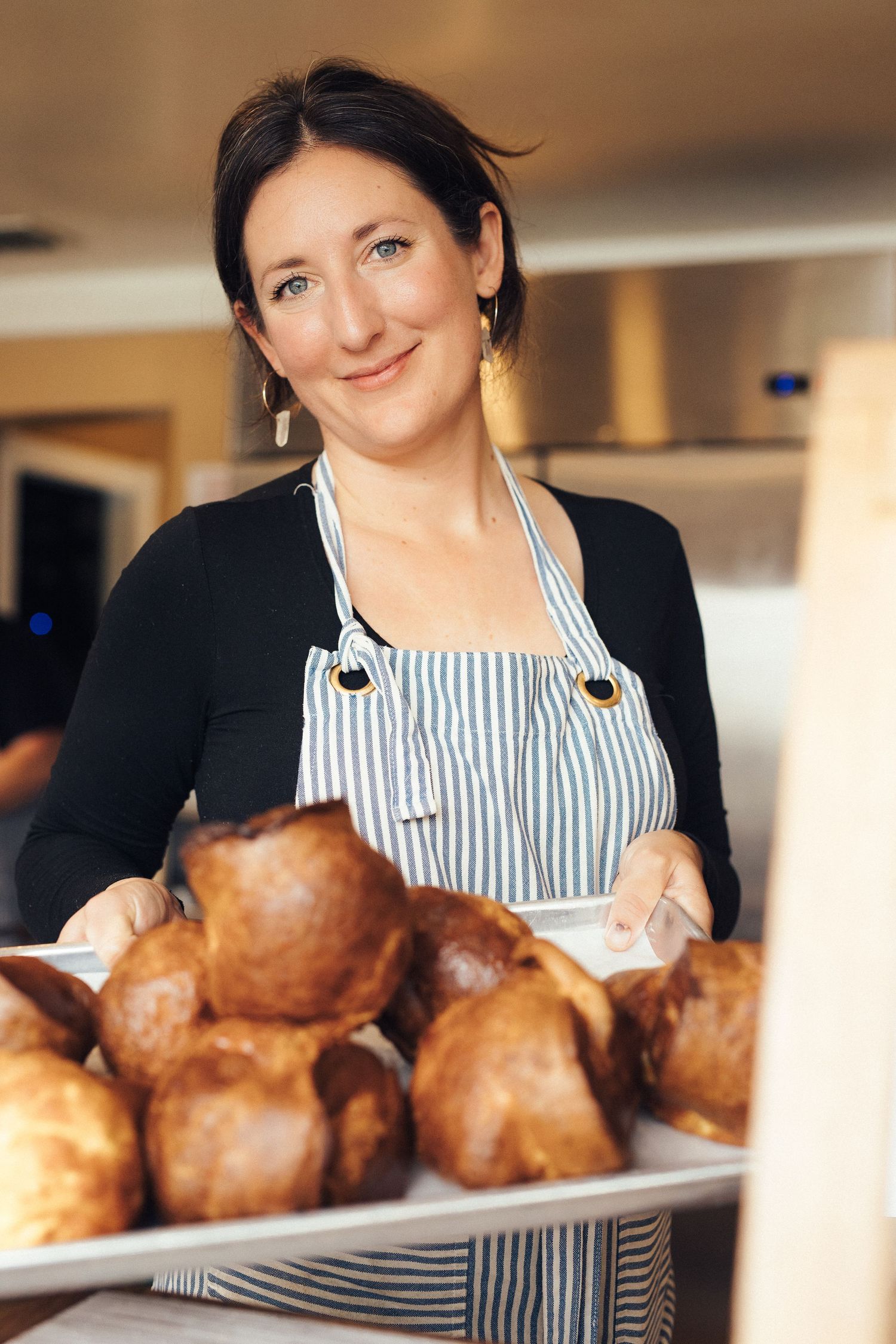 A person in a striped apron displays freshly baked Yorkshire puddings on a serving platter.