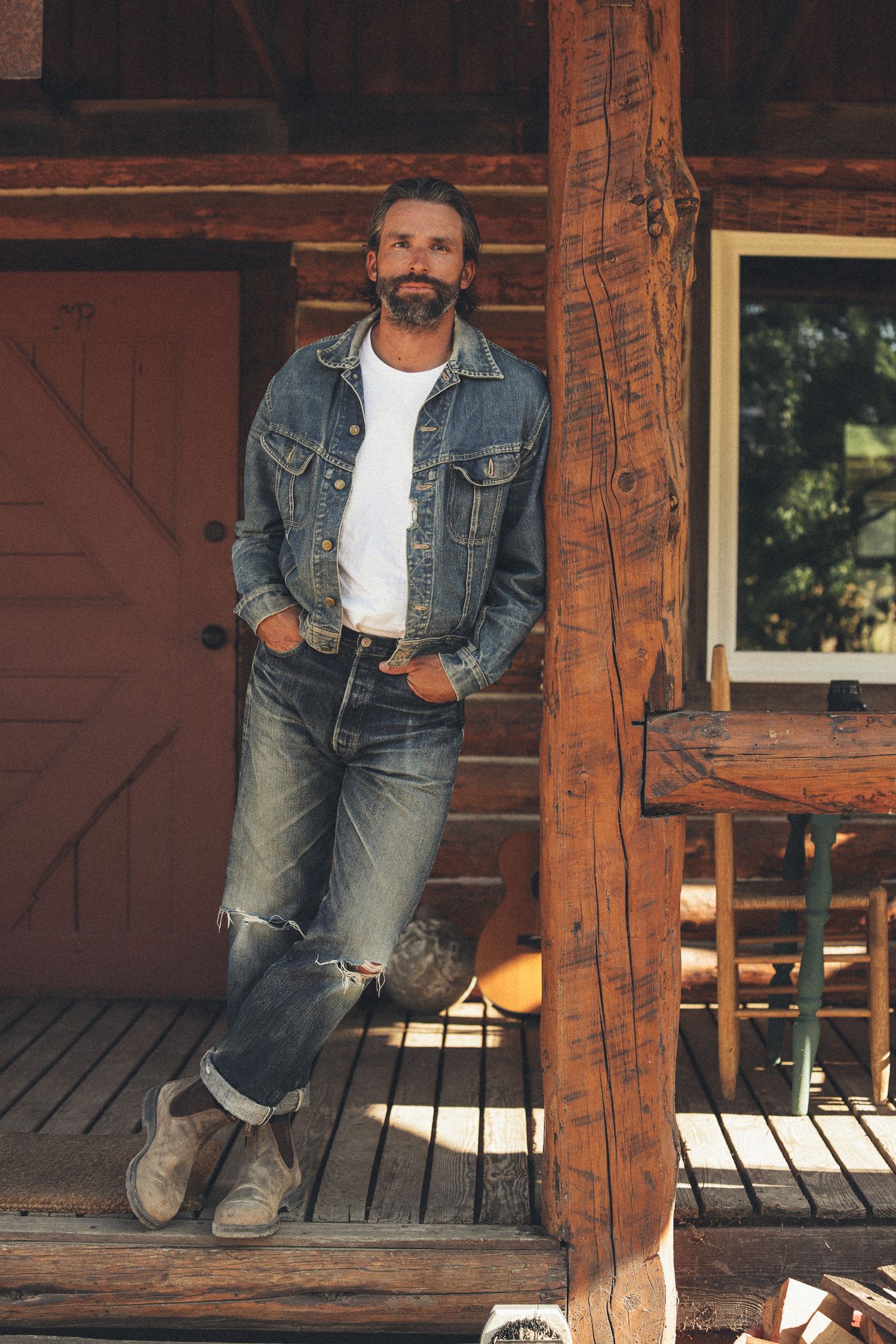 Person in casual denim outfit sitting on rustic wooden porch in warm sunlight.