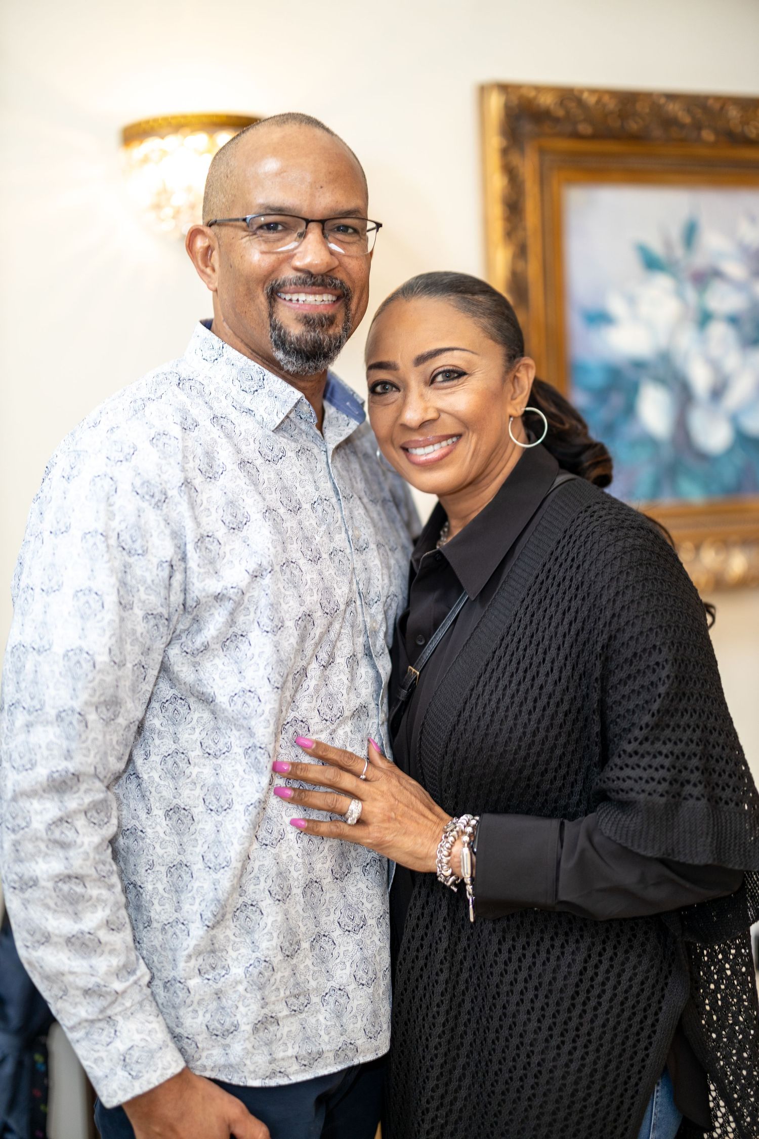 A couple posing together indoors, wearing chic outfits and smiling warmly.