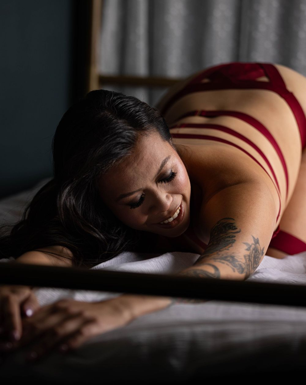 Woman on bed wearing red lingerie photographed by boudoir photographer.