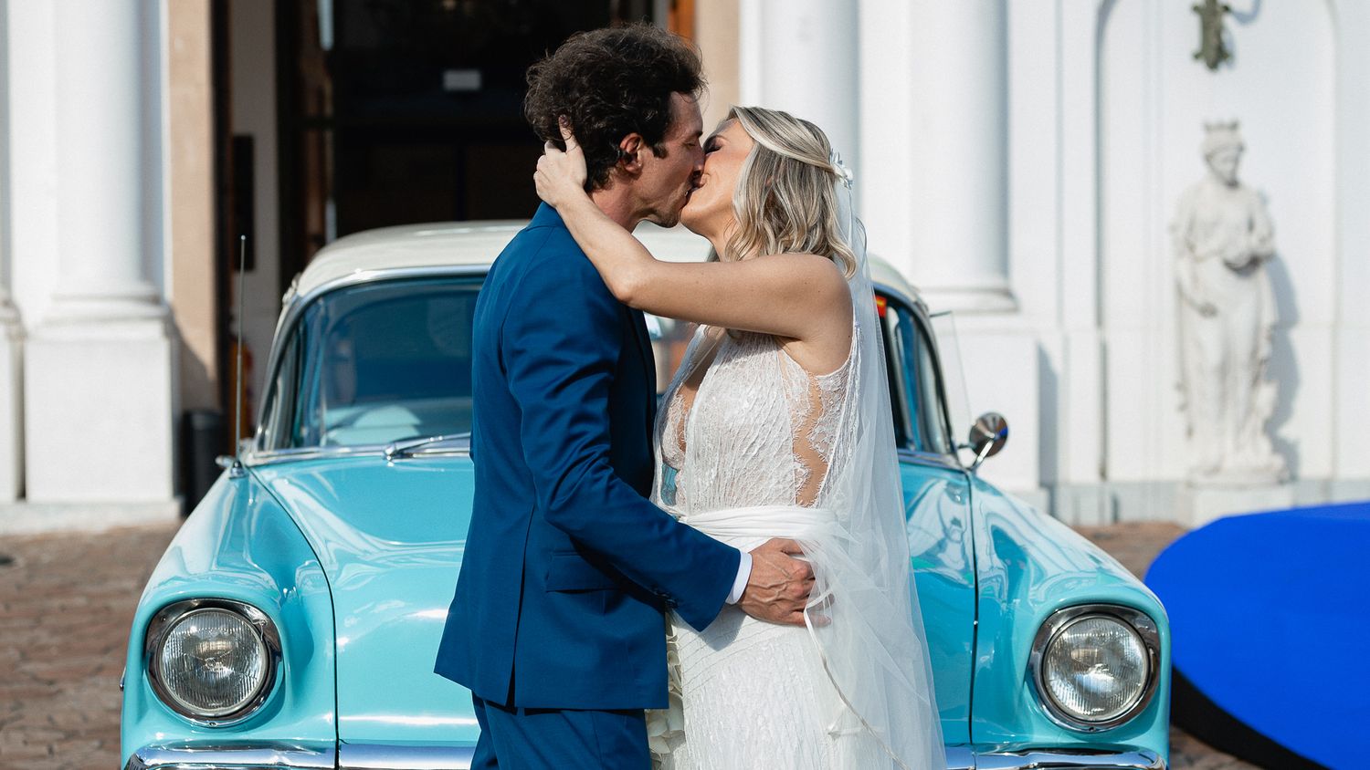 Vintage turquoise car adorned with wedding decorations parked outside a classic building.