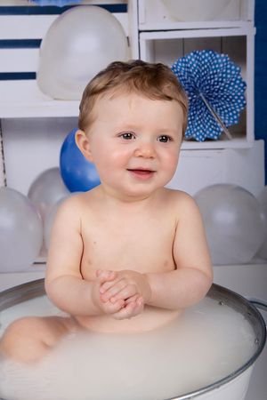 Happy baby in milk bath with blue and white balloon decorations.
