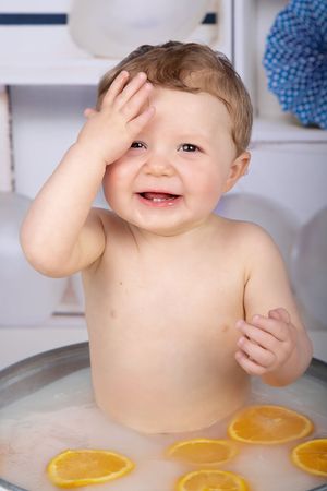 Joyful baby in milk bath with orange slices and blue decor.
