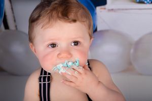 Close up of baby eating cake with frosting on face during cake smash photo session.