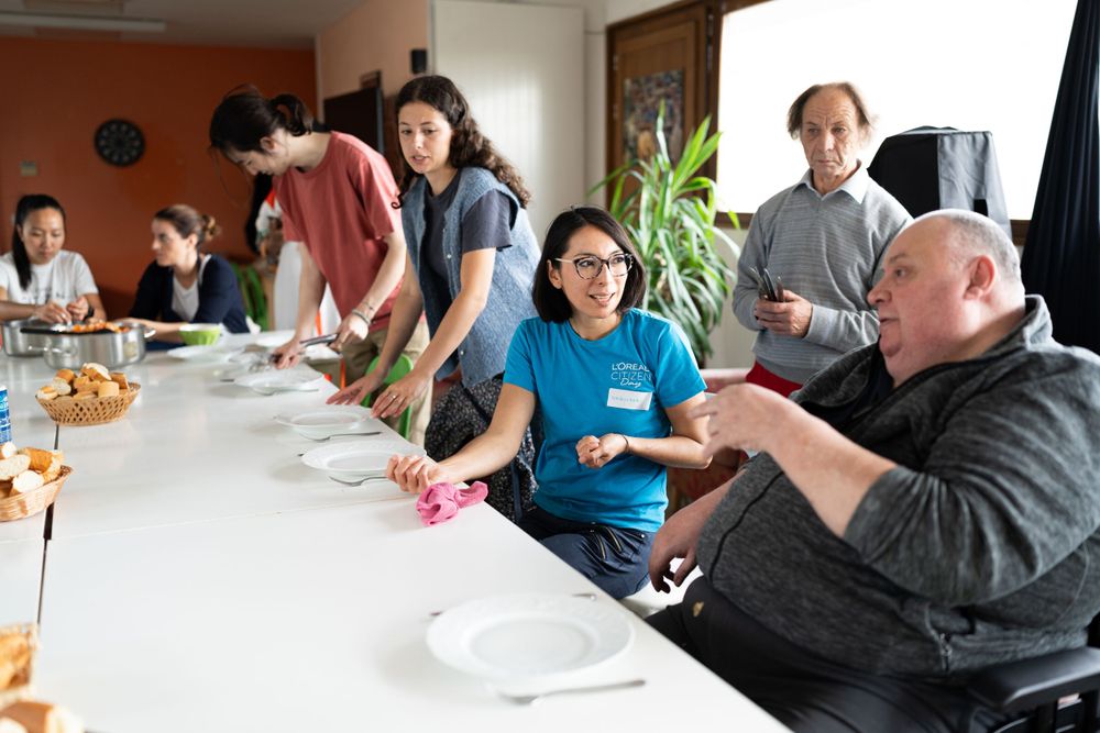 People gather around a long white table during a meal or meeting in a casual indoor setting.