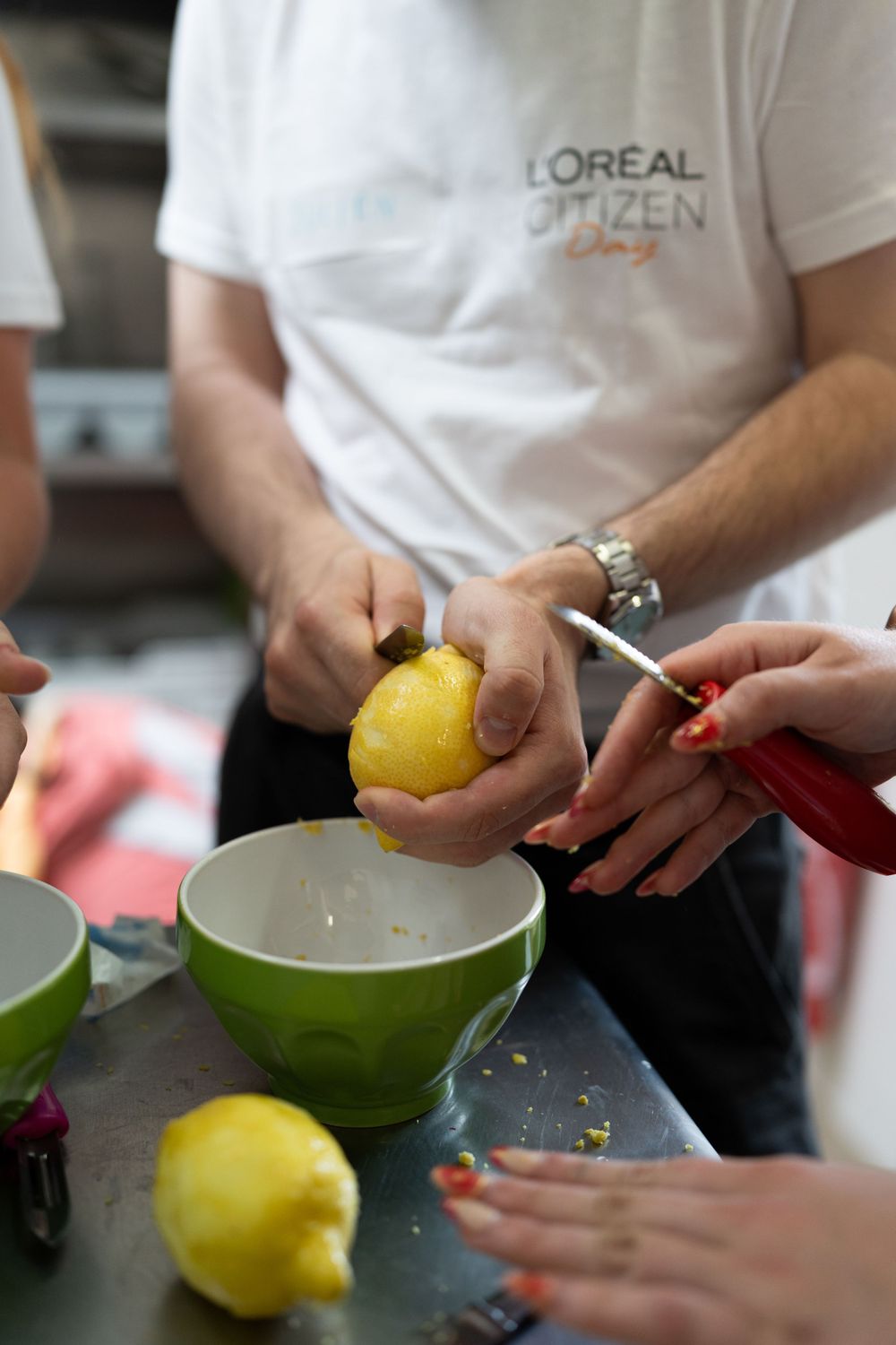 Person wearing a L'Oreal uniform holds a lemon while working in a kitchen with green bowls and cooking tools.
