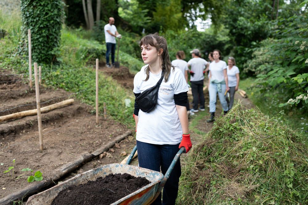 Volunteers working together in garden rows on a hillside during a community service project in lush green surroundings.