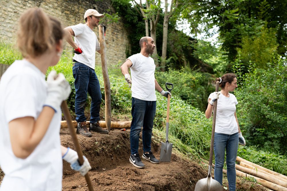 A group of volunteers in white t-shirts work together planting and gardening in a lush outdoor community garden.