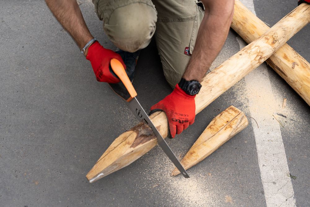 Person wearing red gloves using a handsaw to cut a piece of wood on concrete floor.
