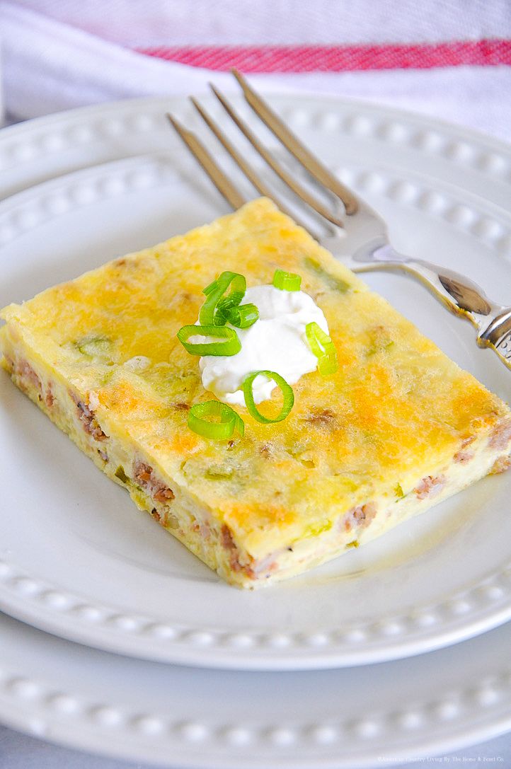 Breakfast casserole square topped with melted cheese, sour cream and green onions on a white plate.