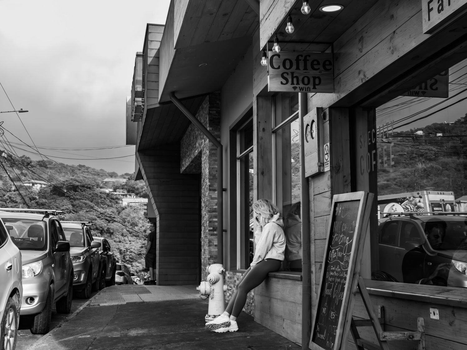Black and white street view of a coffee shop storefront with parked cars on a cloudy day.