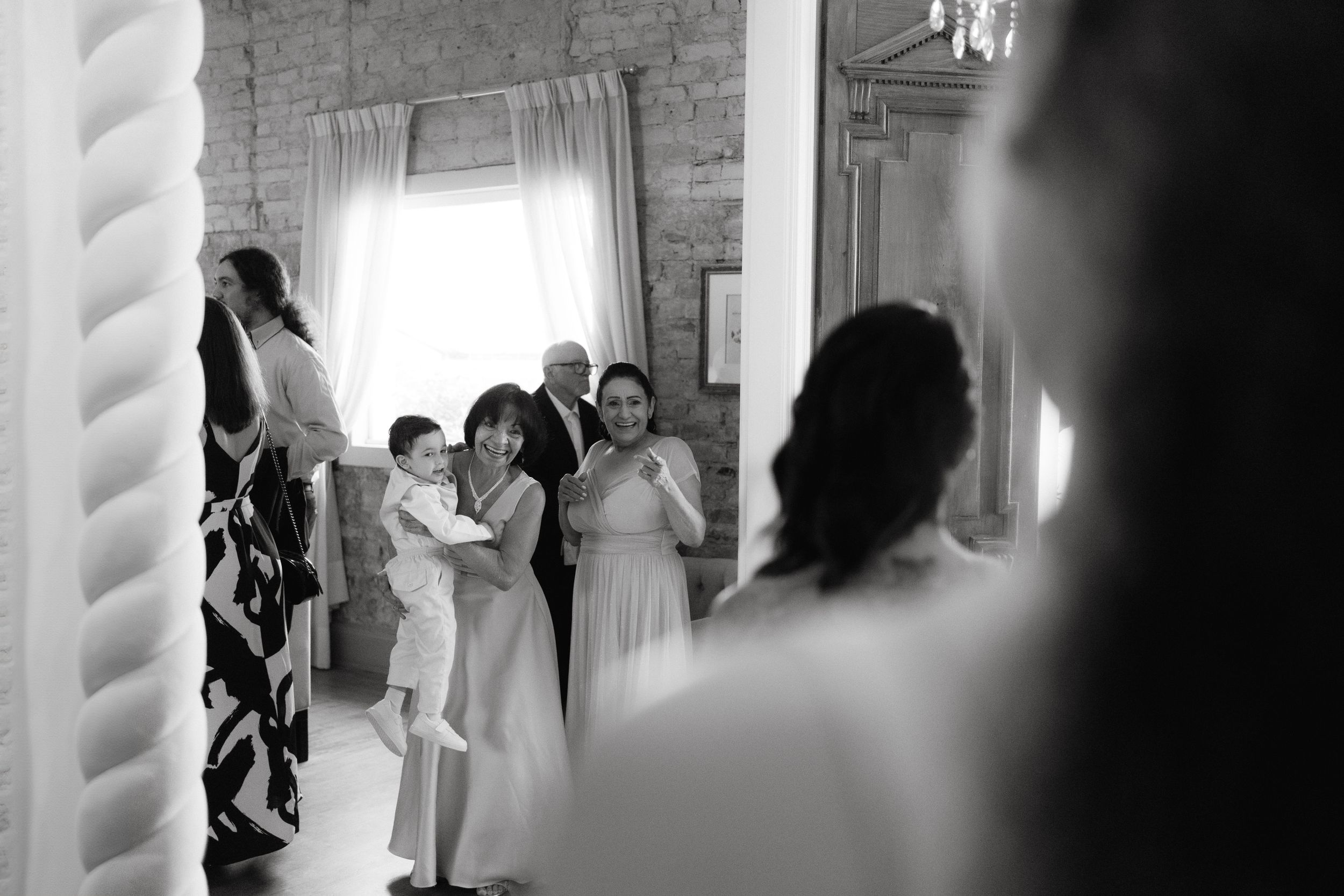 Black and white image capturing wedding guests through doorway during celebration.