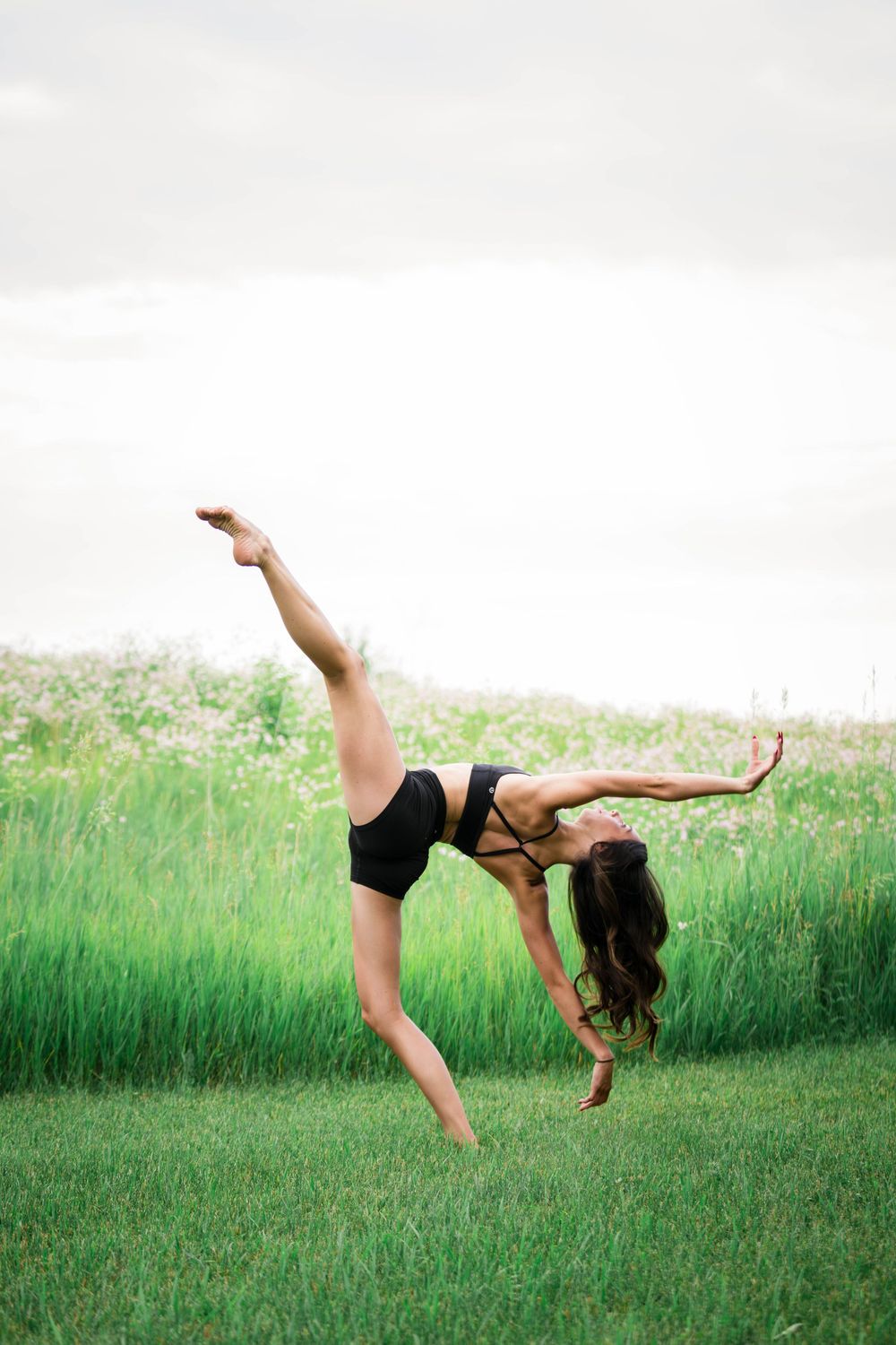 Flexible dancer in black leotard performing a back walkover on green grass field outdoors.